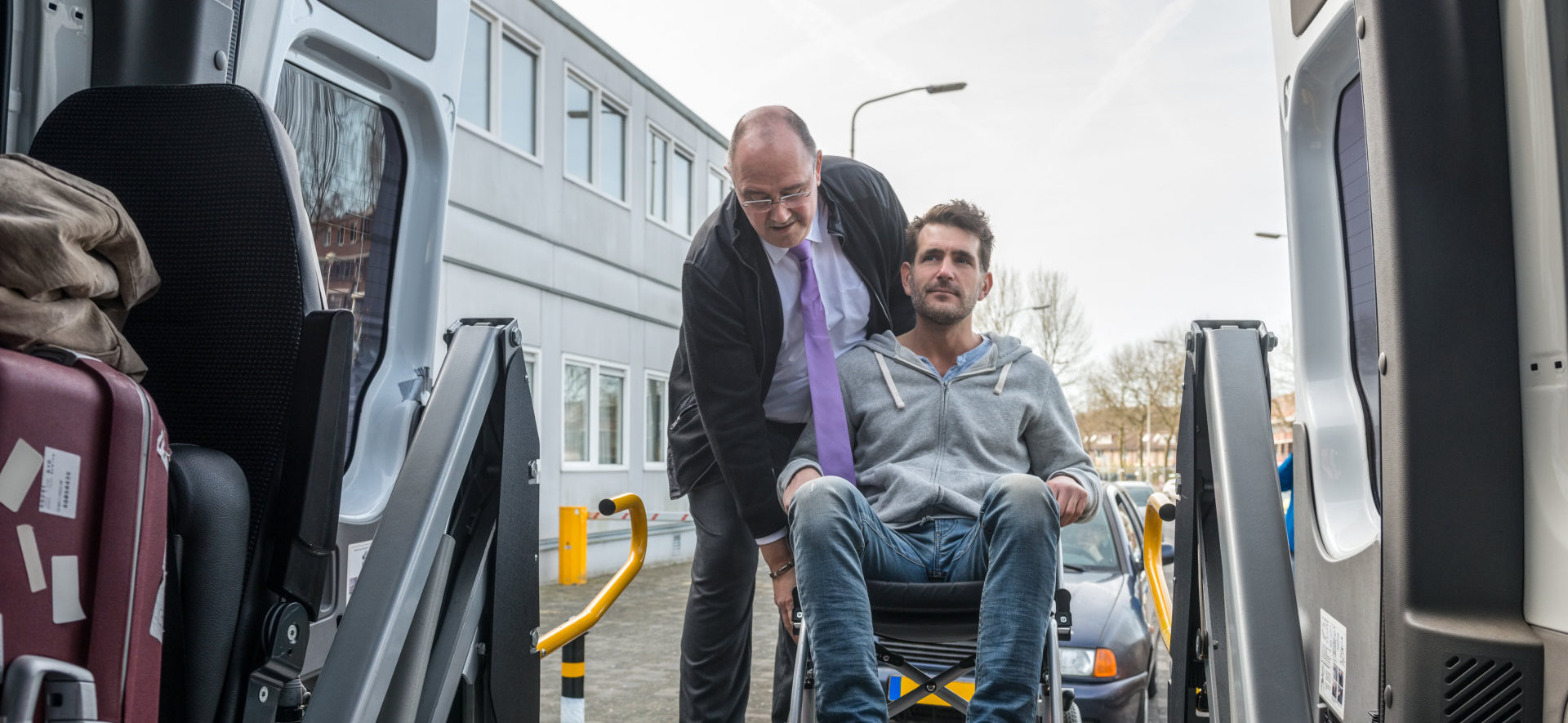 man lifting the wheelchair of the disable adult to get inside the car